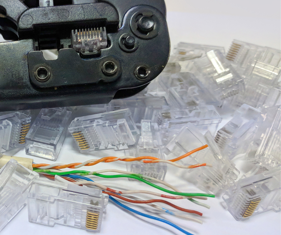A close-up, elevated shot shows a black crimping tool with an RJ45 connector inserted, surrounded by a scattered pile of clear RJ45 connectors. In the foreground, a length of twisted-pair Ethernet cable with exposed, untwisted wires in various colors (orange, white/orange, green, white/green, blue, white/blue, brown, white/brown) lies next to some connectors. custom cable 