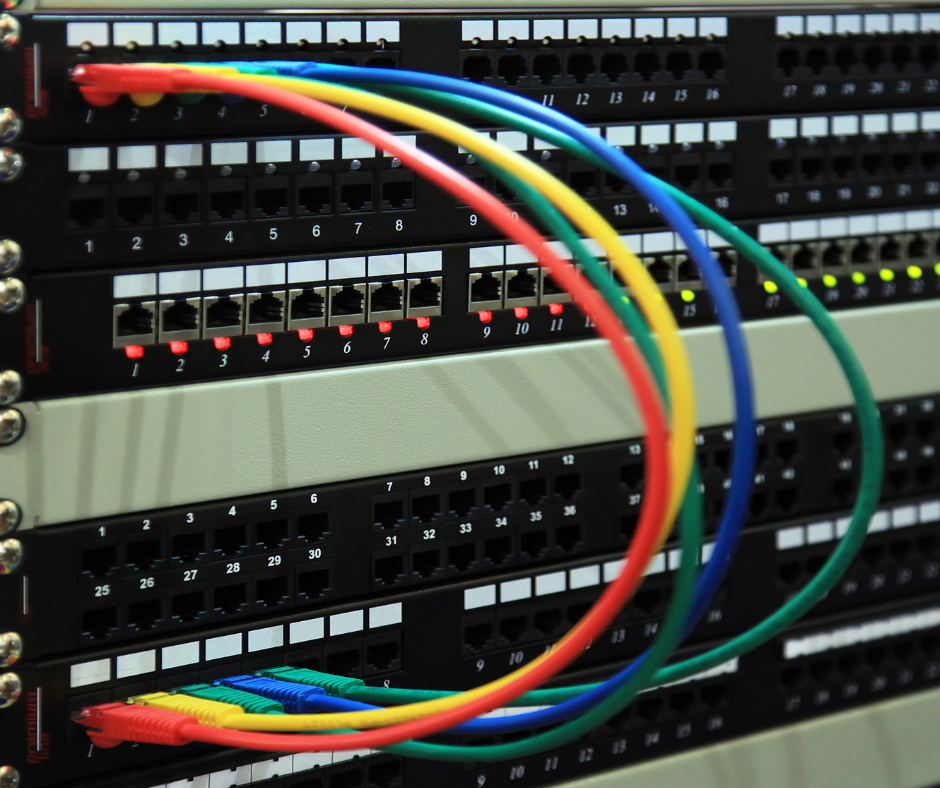 Close-up of a rack-mounted network patch panel with multiple colorful Ethernet cables (red, yellow, green, blue) plugged into its ports, organizing connections in a data center or server room.