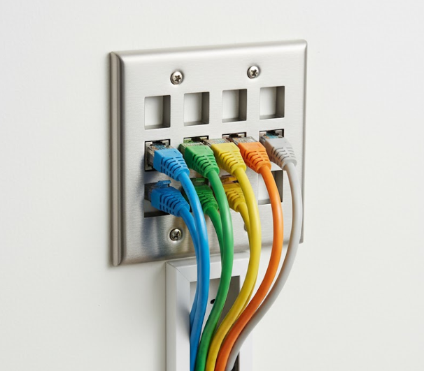 Close-up of a brushed stainless steel wall plate (double gang) with eight square openings. Five colorful Ethernet cables (RJ45, specifically blue, green, yellow, orange, and gray) are plugged into keystone jacks mounted in the lower row of the plate, extending down and out of the frame. The plate is secured to a white wall with four visible screws.